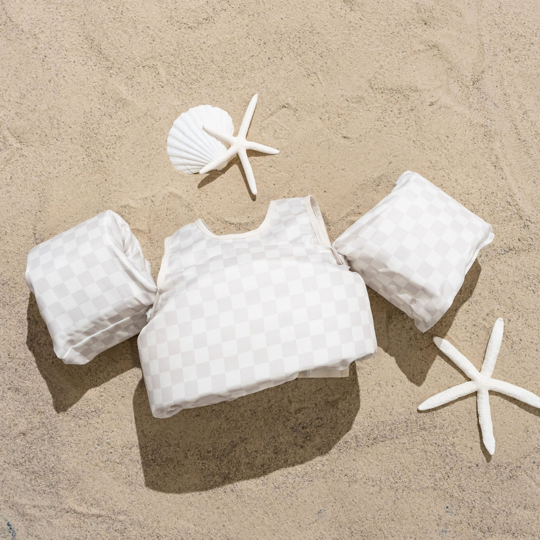 Neutral Checkered Kids Float by Drip Floats displayed on sand with starfish