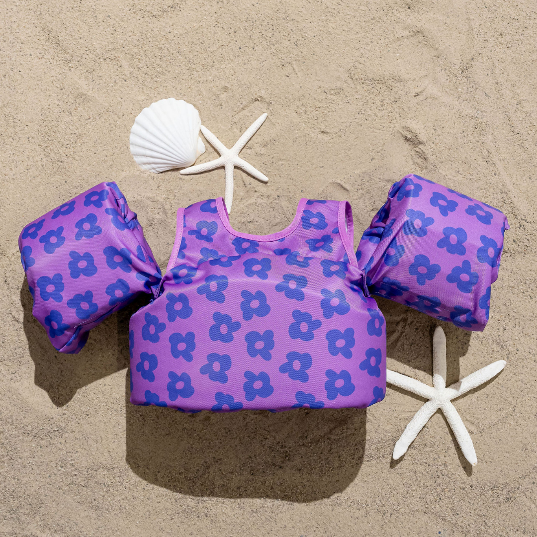 Purple Flower Power kids swim float with floral print displayed on sand